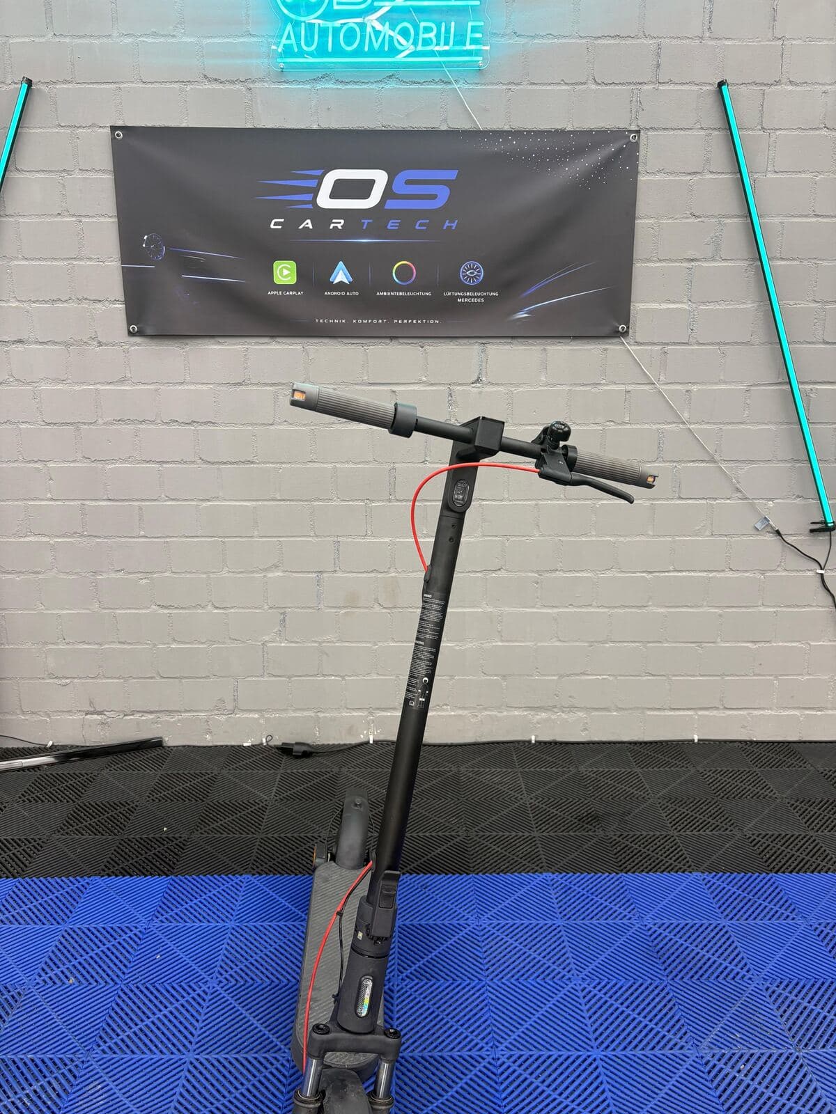 Reparierter E-Scooter vor dem OS CarTech Banner in der Werkstatt